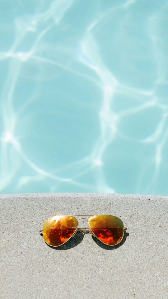 gold framed orange lens Aviator-style sunglasses beside pool